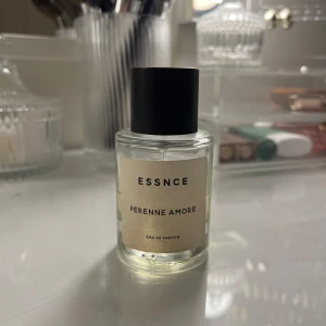 Essnce Perenne Amore Eau de Parfum - Säljer en elegant flaska av Essnce Perenne Amore Eau de Parfum. Flaskan är genomskinlig med en enkel, stilren design och har en svart kork. Doften är subtil och sofistikerad, perfekt för den som söker något unikt.