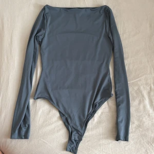 Grå body från HM - Säljer en stilren grå långärmad bodysuit från H&M. Perfekt för lager-på-lager eller att bära som den är. Den har en enkel design med rund hals och är tillverkad i ett mjukt och stretchigt material.