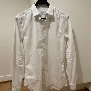 Vit skjorta från Eton - Säljer en stilren vit skjorta från Eton i super slim passform. Skjortan har långa ärmar och knappar framtill. Perfekt för en elegant look. OBS: Sprättat upp sömmarna vid ryggen (se bild 4) vilket ger totalt 4 cm mer vid midjan. Måtten är, Bröst: 104 cm Midja: 92+4 cm Ärm: 90 cm Längd: 76 cm Se även Etons storleksguide för måtten :) Originalpris: 1700kr 