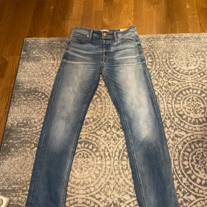 Blå jeans från Jack & Jones strl 28/32 - Snygga blå jeans från Jack & Jones med en klassisk femficksdesign. De har en bekväm passform och är tillverkade i slitstarkt denim. Perfekta för en avslappnad stil.