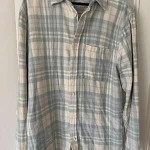 Rutig skjorta från Zara - Snygg rutig skjorta från Zara i ljusblått och vitt. Skjortan har långa ärmar och en klassisk krage. Perfekt för en avslappnad stil med knappar framtill och en bröstficka.