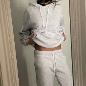 Grå hoodie med byxor  - Säljer en mysig grå hoodie med luva och dragsko, gråa mjukisar kommer med. Tröjan har en stor ficka framtill och är perfekt för en avslappnad stil. Passar bra till både hemmamys och vardagsäventyr. XS på hoodies dene lång även mjukisar storlek Xs!
