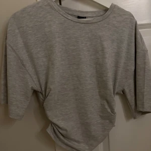 Grå t-shirt från Gina Tricot - Säljer en mjuk och bekväm gråmelerad t-shirt från Gina Tricot. Den har en avslappnad passform och trekvartsärmar, perfekt för en casual look. T-shirten är i ett mjukt material som känns skönt mot huden.