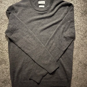 Grå merinoulltröja från These Glory Days - Säljer en stilren grå tröja från These Glory Days i mjuk och lyxig merinoull. Tröjan har en klassisk rund hals och långa ärmar, perfekt för kyligare dagar. Passar både till vardags och mer uppklädda tillfällen.