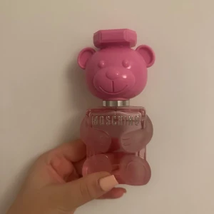 Rosa parfymflaska från Moschino - Säljer en unik parfymflaska från Moschino formad som en nallebjörn. Flaskan är rosa med en genomskinlig kropp och ett rosa huvud som lock. Perfekt för den som älskar lekfull design och vill ha något speciellt på parfymhyllan. Ny pris ca 950 men säljer för 550!