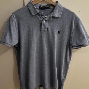 Ljusblå pikétröja Ralph Lauren - Säljer en stilren ljusblå pikétröja från Ralph Lauren i custom slim fit. Tröjan har korta ärmar och en klassisk krage med knappar. 