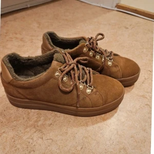 Bruna sneakers från Gant - Snygga bruna sneakers från Gant i mocka med snörning och foder i päls. Perfekta för kyligare dagar med sin varma insida. Skorna har en robust sula och metallöglor för snörena.