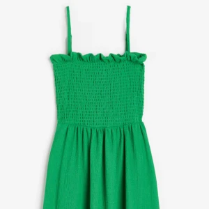 Grön klänning med smockdetaljer - Snygg grön klänning med smala axelband och smockdetaljer upptill. Perfekt för sommarens varma dagar. Klänningen har en luftig passform och är gjord i ett mjukt material som ger en bekväm känsla. Ett måste i garderoben för en fräsch och stilren look.