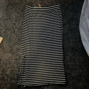 Randig kjol från Holly & Whyte - Snygg långkjol från Holly & Whyte med klassiskt randigt mönster i svart och vitt. Kjolen har en bekväm passform och är perfekt för både vardag och speciella tillfällen. Den är tillverkad i ett mjukt och följsamt material.