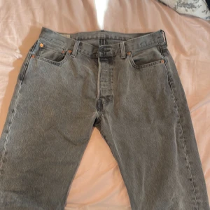 Grå jeansbyxor från Levi's - Snygga grå jeansbyxor från Levi's med klassisk femficksdesign och knappgylf. Byxorna har en rak passform och är perfekta för en avslappnad stil. Levi's ikoniska läderpatch syns på baksidan.
