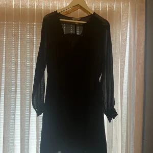Svart klänning från H&M - Elegant svart klänning från H&M med långa ärmar i ett transparent material. Perfekt för en stilren look. Klänningen har en enkel design som gör den lätt att matcha med olika accessoarer.