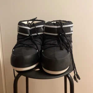 Svarta Moon Boots - Snygga och varma svarta Moon Boots med vit sula och snörning. Perfekta för kalla vinterdagar med sin ikoniska design och bekväma passform.