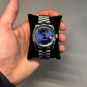 Silverfärgad klocka med blå urtavla - Elegant klocka med en blå urtavla och datumvisning. Armbandet är i silverfärgad metall och har en klassisk design. Perfekt för den som söker en stilren och tidlös accessoar.