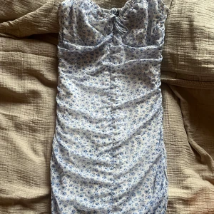 Blommig klänning från H&M - Söt blommig klänning från H&M i vitt och blått. Klänningen har smala axelband och en knytning framtill. Perfekt för varma dagar med sitt lätta och luftiga material. Säljer pga för stor och kom ej till användning 