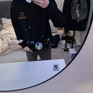 Svart hoodie från Gallery Dept. - Säljer en svart hoodie från Gallery Dept. med färgstänk och tryck på bröstet. Hoodien har en klassisk design med justerbar huva och ribbade muddar. Står storlek S men skulle säga att den är M.