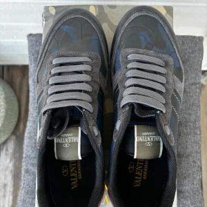 Valentino Rockrunner - Snygga Valentino Rockrunner sneakers med ett coolt camouflagemönster i grått och blått. Skorna har en unik kombination av mocka och skinn, med en vinröd detalj på hälen. Sälja i befintlig skick.Perfekta för att ge din stil en edgy touch.
