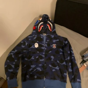 Blå hoodie från BAPE & PSG - Säljer en cool blå camo hoodie från BAPE och Psg  köpt för 1149 Använd 3 gånger Storlek M