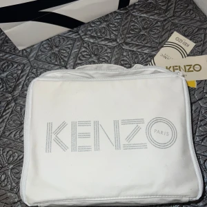 Vit necessär från Kenzo med tillhörande filt  - Säljer en stilren vit necessär från Kenzo med dragkedja och tryckt logotyp. Insidan har ett mönster med tigrar i grått. Perfekt även för att hålla ordning på bebisens saker. Helt ny! Nypris 1699kr 