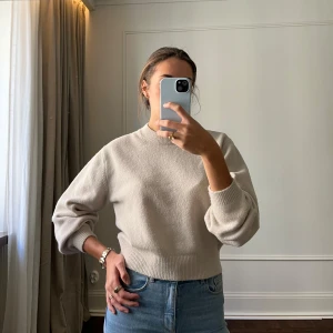 Beige stickad tröja från & Other Stories - Säljer en stilren beige stickad tröja från & Other Stories. Tröjan har en rund halsringning och långa ärmar med ribbade muddar. Perfekt för en avslappnad och trendig look. Passar bra till jeans eller kjol.