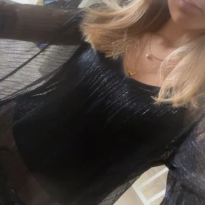 Marinblå festblus - Snygg marinblå glittrig transparent blus med långa ärmar och volangdetaljer. Perfekt för en trendig look. Passar bra över ett linne eller en topp.