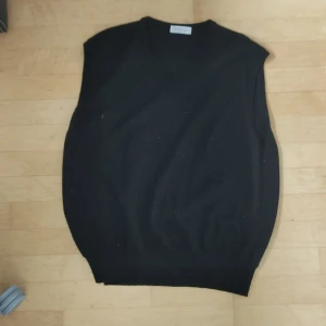 Svart ullväst från Gran Sasso - Snygg svart väst från Gran Sasso i mjukt ullmaterial. Den har en klassisk v-ringad design som passar perfekt för lager-på-lager-stil. Tillverkad i Italien, vilket garanterar hög kvalitet och stil. Perfekt för att hålla värmen med stil under kyligare dagar. Bra skick . Öppen mot bud