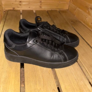 Svarta sneakers från Graceland - Snygga svarta sneakers från Graceland med snörning. De har en stilren design med en helsvart färg och en bekväm sula. Perfekta för en casual look.