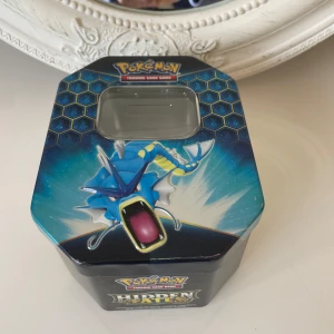 Pokémon Hidden Fates Tin Box - Säljer en Pokémon Hidden Fates plåtlåda med Gyarados-motiv. Perfekt för att förvara dina Pokémon-kort eller andra småsaker. Lådan har en sexkantig form och ett genomskinligt fönster på locket. En samlarfavorit för Pokémon-fans! 🌟.längd på låda är 15,04cm . Höjd på lådan är 7,04cm . Kan möta er i T-Central utanför Åhléns i Stockholm 