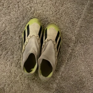 Adidas crazy fast - Säljer ett par Adidas fotbollsskor i vitt med svarta ränder och neongula detaljer. Skorna har en strömlinjeformad design utan snörning för en tight passform. Perfekta för fotbollsplanen!