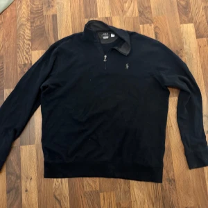 Svart tröja från Ralph Lauren - Säljer en stilren svart tröja från Ralph Lauren med dragkedja vid halsen. Tröjan har långa ärmar och en liten broderad logotyp på bröstet. Köpt för 3000, säljer för den inte kommit till användning 