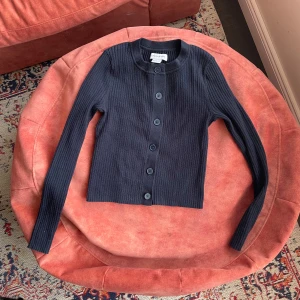 Svart ribbad kofta från Urban Revivo - Säljer en stilren svart ribbad kofta från Urban Revivo. Koftan har långa ärmar och knappar framtill, perfekt för lager-på-lager-stil. Passar både till vardags och mer uppklädda tillfällen.