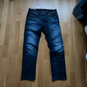 Mörkblå jeans från Jack & Jones - Säljer ett par snygga mörkblå jeans från Jack & Jones. De har en klassisk femficksdesign och en knappgylf. Perfekta för en stilren look. Pris kan sänkas vid snabbt köp
