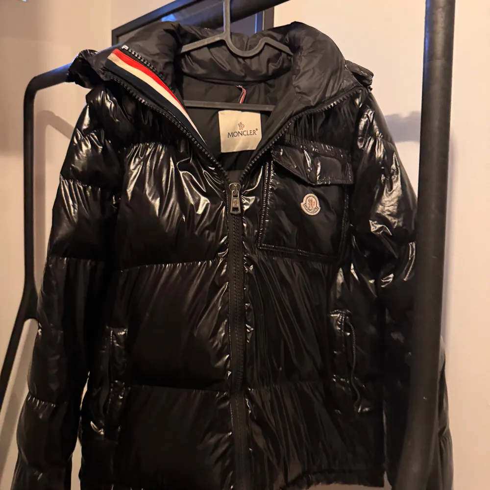 Snygg svart dunjacka från Moncler med glansig finish. Jackan har en dragkedja framtill och en hög krage för extra värme. Perfekt för kyliga dagar. Från 🇨🇳för dom som förstår fast en väldigt bra. Takit.