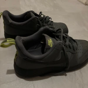 Nike air forces - Snygga svarta Nike sneakers med gröna detaljer och snörning. Perfekta för en sportig look med en klassisk design. De har en låg profil och är bekväma för vardagsbruk.