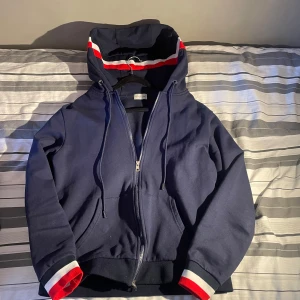 Mörkblå huvtröja från Moncler - Säljer en snygg mörkblå huvtröja från Moncler med dragkedja och feta detaljer på ärmarna samt luvan som verkligen höjer tröjan. Den är sparsamt använd och passar runt 177-185 cm. Inget fel på den, scan funkar och skickas snarast, tveka inte om frågor eller diskutera priset