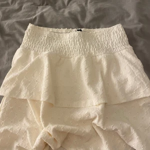 Vit kjol med volangdetaljer - Säljer en söt vit kjol med volangdetaljer och elastisk midja. Kjolen är helt oanvänd och pris går att diskutera.