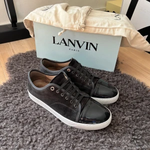 Lanvin uk 10 passar 44/45 - Snygga svarta sneakers från Lanvin med en stilren design. Skorna har en kombination av mocka och skinn med en glansig tå och vita sulor. Perfekta för en trendig look. Topp skick inga defekter allt og tillkommer box och dustbag priset går att diskutera lite grann.