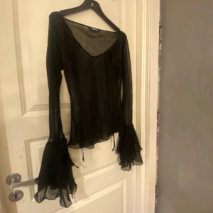 Svart transparent blus från ONLY - Snygg svart transparent blus från ONLY med långa ärmar och volangdetaljer vid ärmslut och nederkant. Perfekt för en stilfull look.