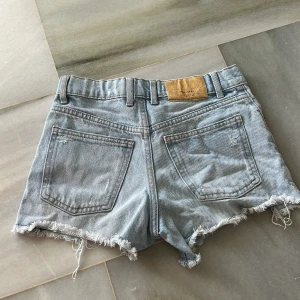 Ljusa jeansshorts från Zara - Säljer ett par ljusa jeansshorts från Zara med fransiga kanter och slitna detaljer. Jeansshortsen är i storlek 10Y/140