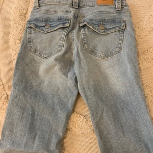 Ljusblå bootcut jeans från Gina tricot - Snygga low waist ljusblå bootcut jeans. De har en klassisk femficksdesign med knappar på bakfickorna och en bekväm passform. Perfekta för en avslappnad stil.