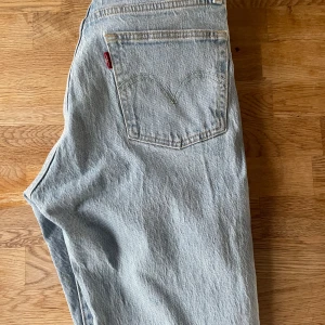 Ljusblåa jeans från Levi's - Säljer ett par klassiska ljusblåa 501 jeans från Levi's med knappgylf. De har en avslappnad passform och är perfekta för en casual look. Levi's ikoniska läderpatch finns på baksidan av midjan. Innerbens måttet är 62.