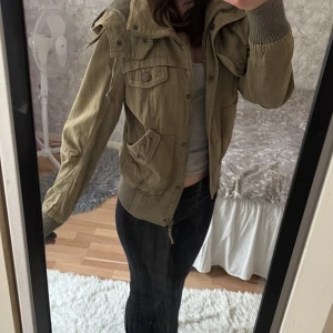 Grön jacka med huva - Säljer en olivgrön jacka med huva och dragkedja. Jackan har flera fickor med knappar. Perfekt för höst och vår! Den är i Storlek M men passar mig som använder XS-S🫶🏼