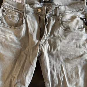 Grå jeans från Replay - Snygga grå jeans från Replay med dragkedja och knapp framtill. Klassisk femficksdesign med broderad detalj på bakfickan. Perfekta för en stilren look. Storlek 31, Färgen är lite missfärgad 