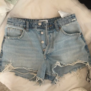 Zara shorts  - Säljer ett par blå jeansshorts från zara i strl 34 med fransiga kanter och knappar framtill. Shortsen har en sliten look med en trasig detalj på bakfickan. Använda max 2 ggr 💞