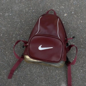 Vintage Vinröd ryggsäck från Nike - Vintage 90 tals Snygg vinröd ryggsäck från Nike med vit logga på framsidan. Väskan har en dragkedja och justerbara axelremmar. Botten är genomskinlig med en röd Nike-logga. Perfekt för att bära dina saker med stil. Har litet slitage, se bild 4. Fråga gärna om fler foton.