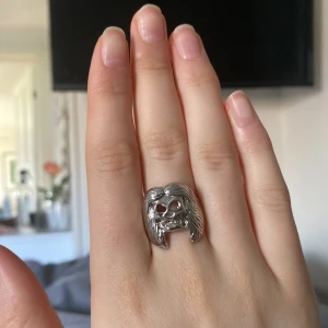 Silverfärgad ring  - Snygg och unik ring i silverfärg med en detaljerad döskalle som motiv. Perfekt för att ge en djärv touch till din stil. Ringen har en robust design och är ett statement-smycke för den modiga.