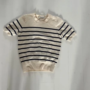 Randig kortärmad tröja från Zara - Säljer en stilren beige och svart randig tröja från Zara. Tröjan har korta ärmar och en rund halsringning, perfekt för en avslappnad look. Passar bra till jeans eller kjol!