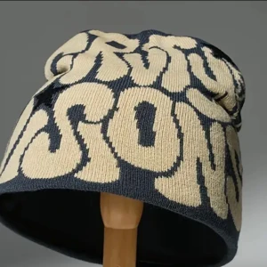 Beige och svart mössa med text - Snygg mössa i beige och svart med stor textdesign. Perfekt för att hålla stilen under kyliga dagar. Den har en avslappnad passform och är tillverkad i ett mjukt material för extra komfort.