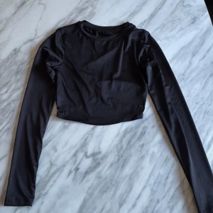 Svart långärmad croppad topp - Snygg svart croppad topp med långa ärmar och unik snörningsdetalj på ryggen. Perfekt för en trendig look.