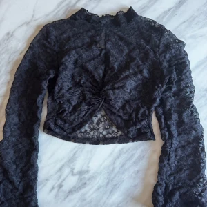 Svart spetsblus med knytning - Elegant svart spetsblus med långärmad design och knytning framtill. 