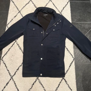 J.lindberg Field jacket  - Säljer nu min j.lindberg jacka i top skick, helt slutsåld överallt! (Nypris runt 3500kr) Storlek S passar M, modellen 182-ca 65kg. Obs lite blöt i höger hörnet därav lite mörkare på den sidan. Skriv för fler frågor!